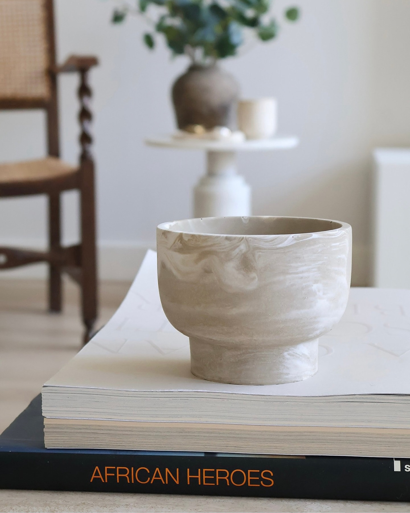 A pale marbled handmade vessel styled on stacked art books.