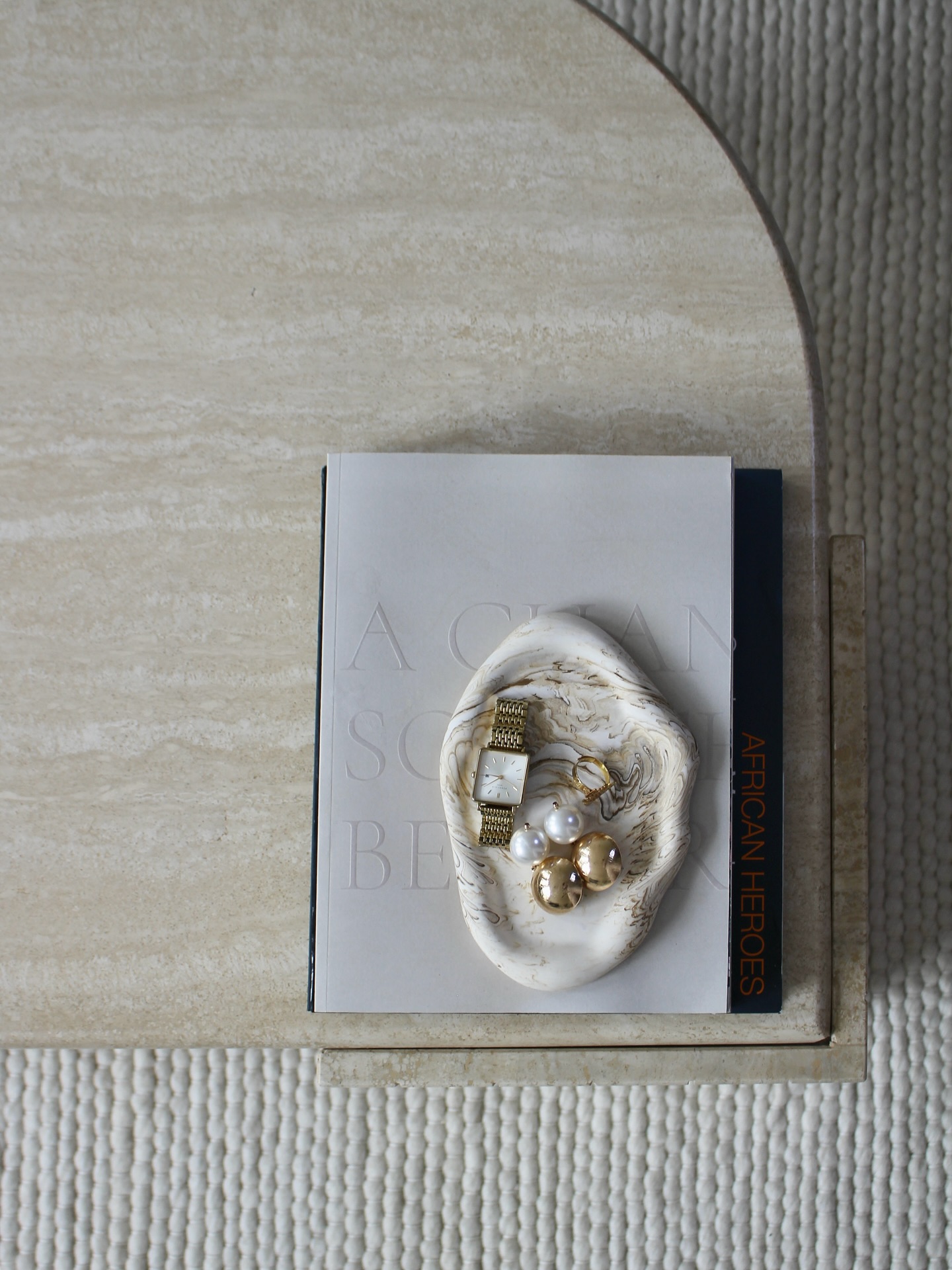 The Adiam marbled tray holding jewelry on a book.