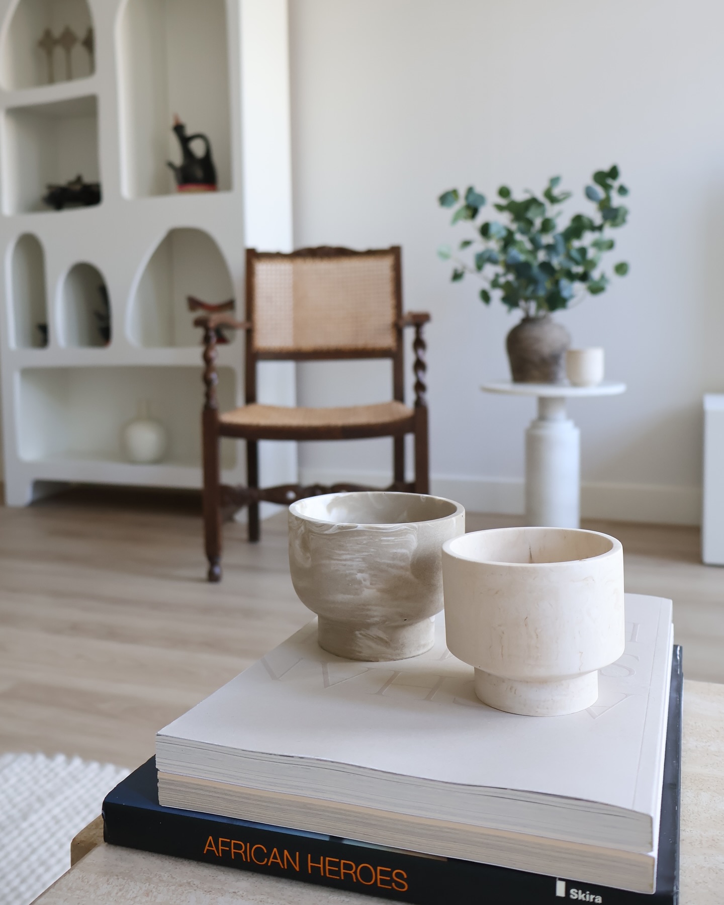 Two handmade marbled vessels styled on art books in a calm pale interior.