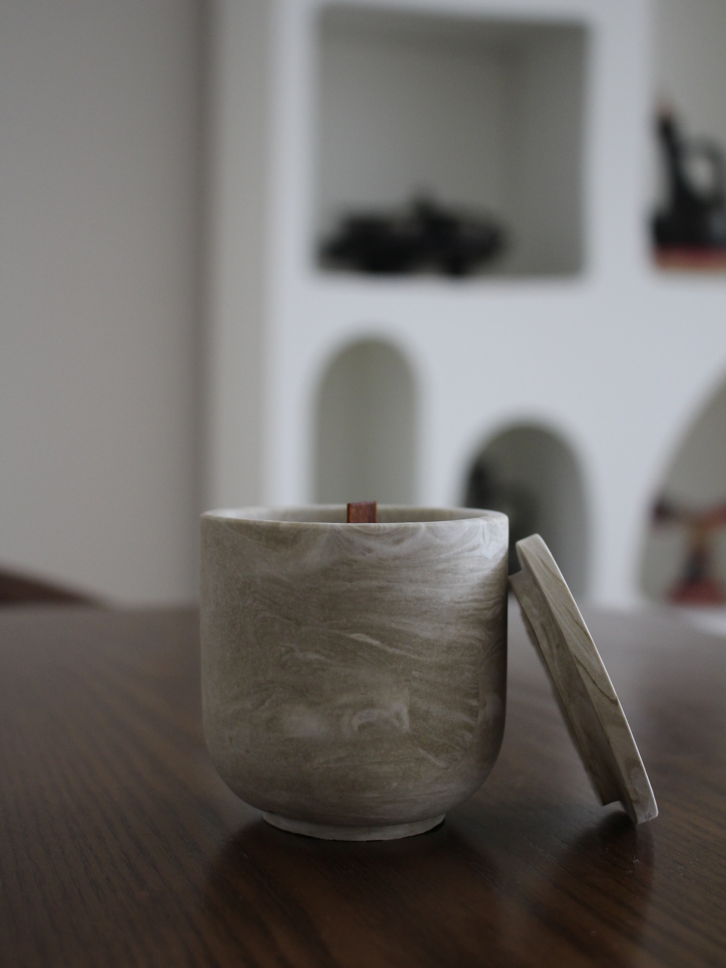 The Tigist marbled vessel with its lid resting beside it on a dark wood surface.